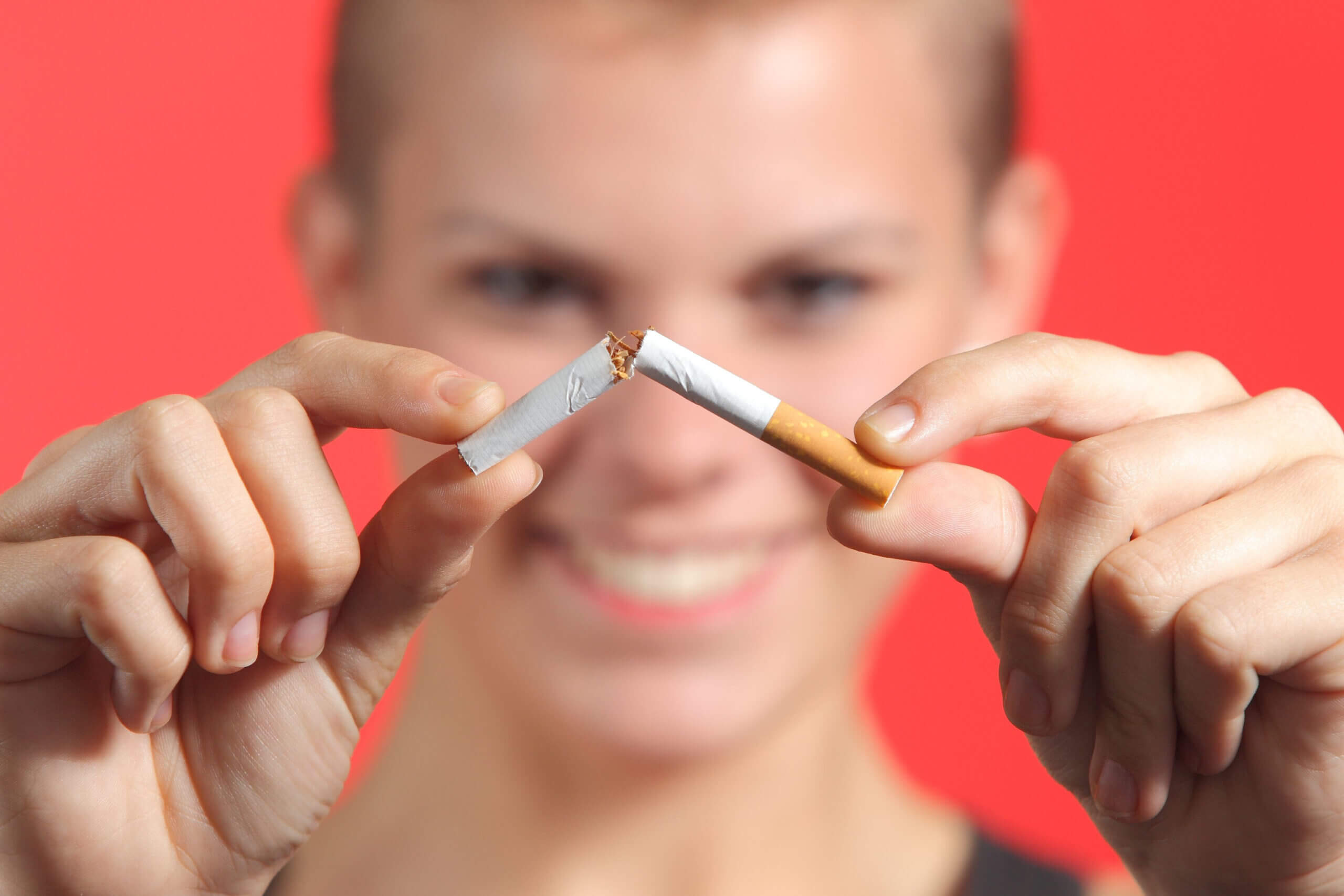 Woman breaking a cigarette on a red background